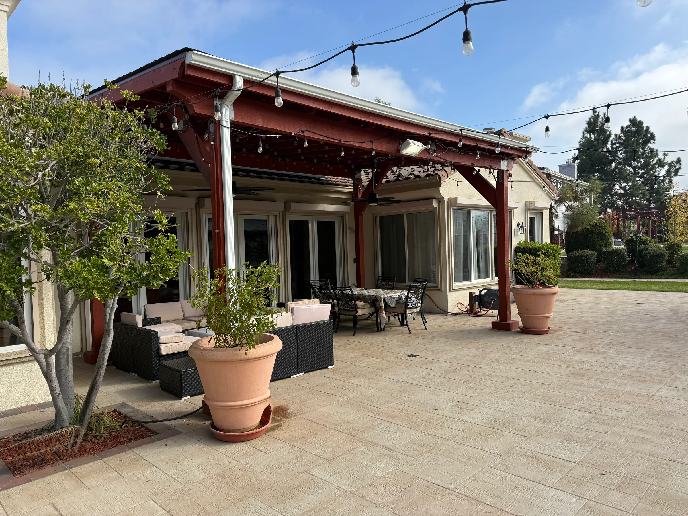 Covered patio with stained redwood posts and beams, string lighting, and a large paver patio