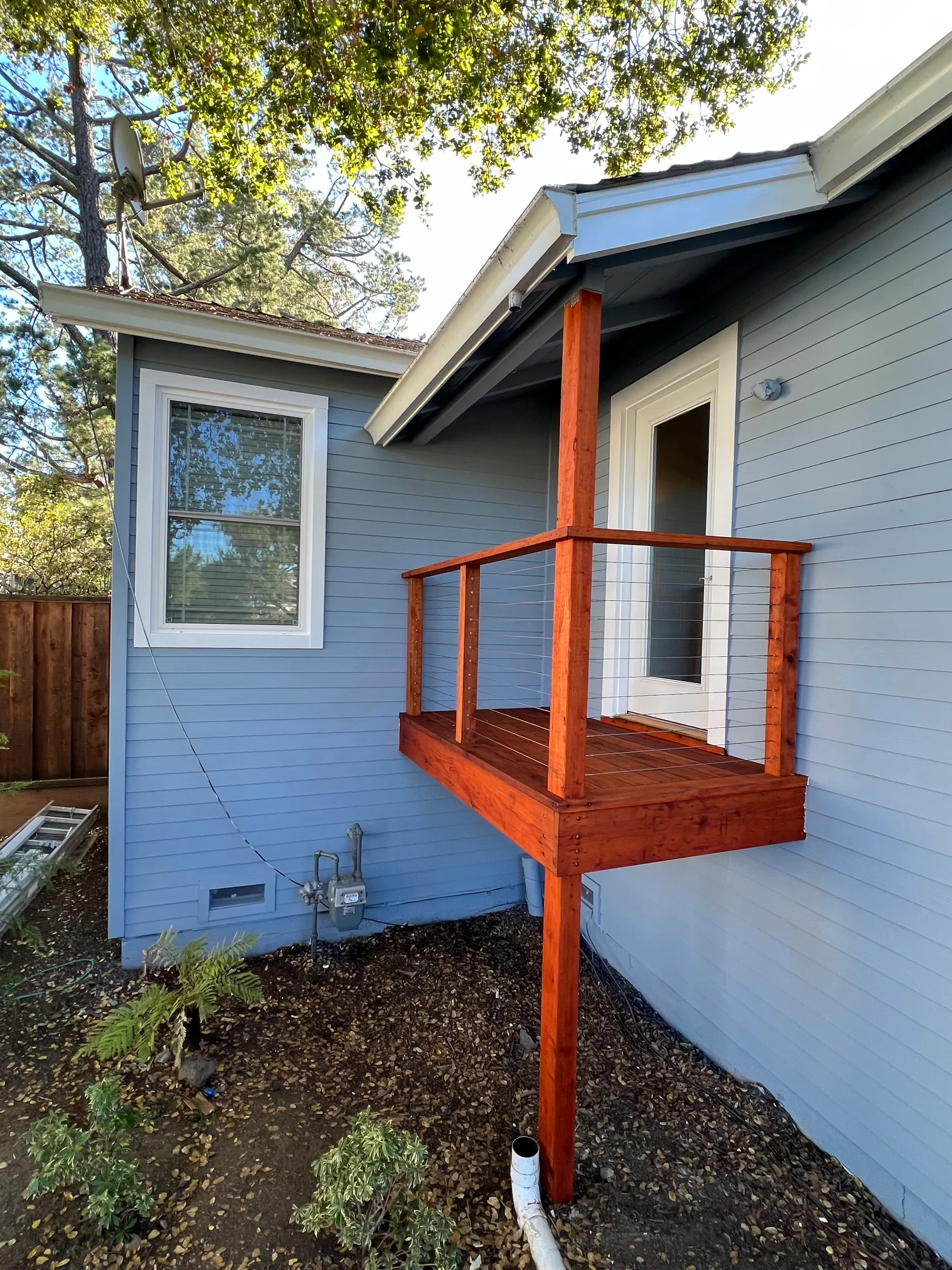 Elevated redwood entry landing with stainless cable railing against new gray lap siding