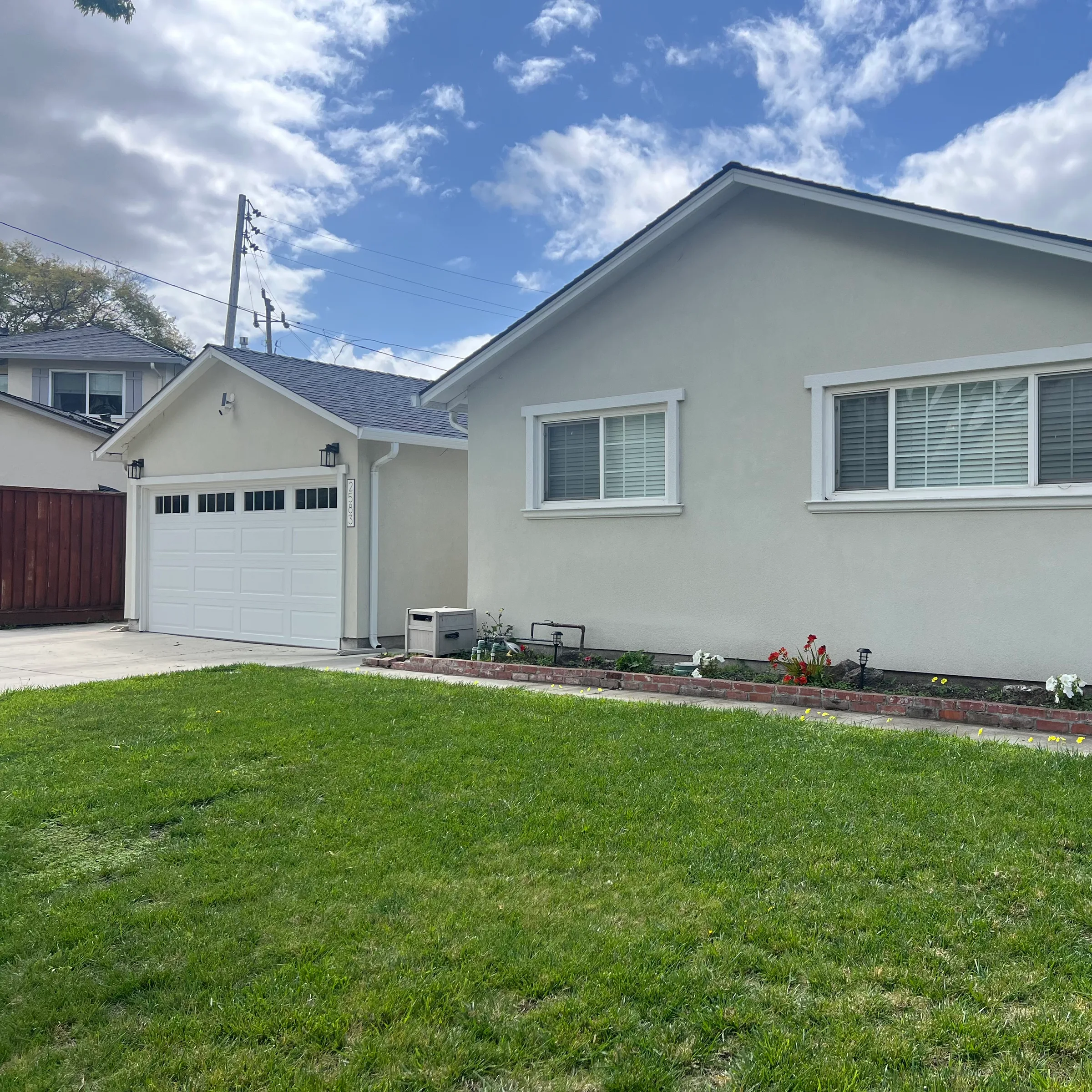 Ranch home front elevation with fresh stucco, a new white garage door, and brick planter edging