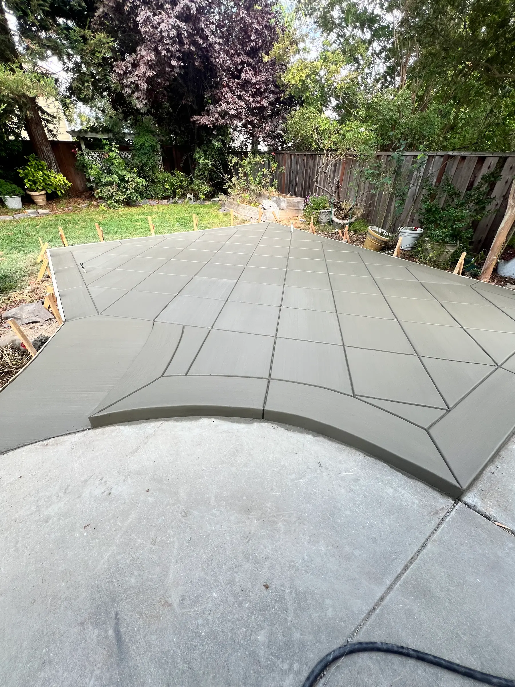 Backyard concrete patio in a sage finish with scored diamond panels and a curved front edge