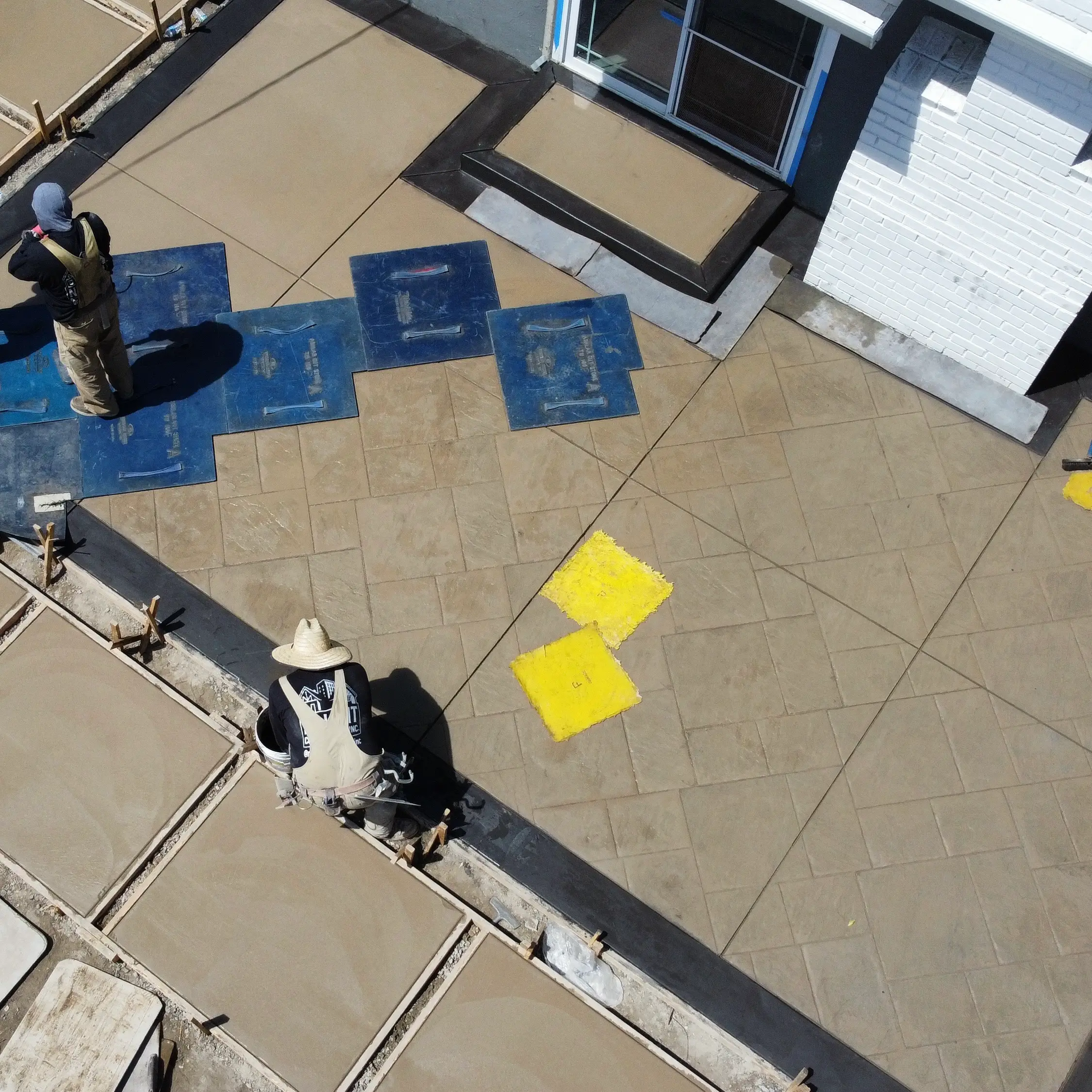 Aerial view of a crew pressing texture mats into a freshly poured stamped concrete patio