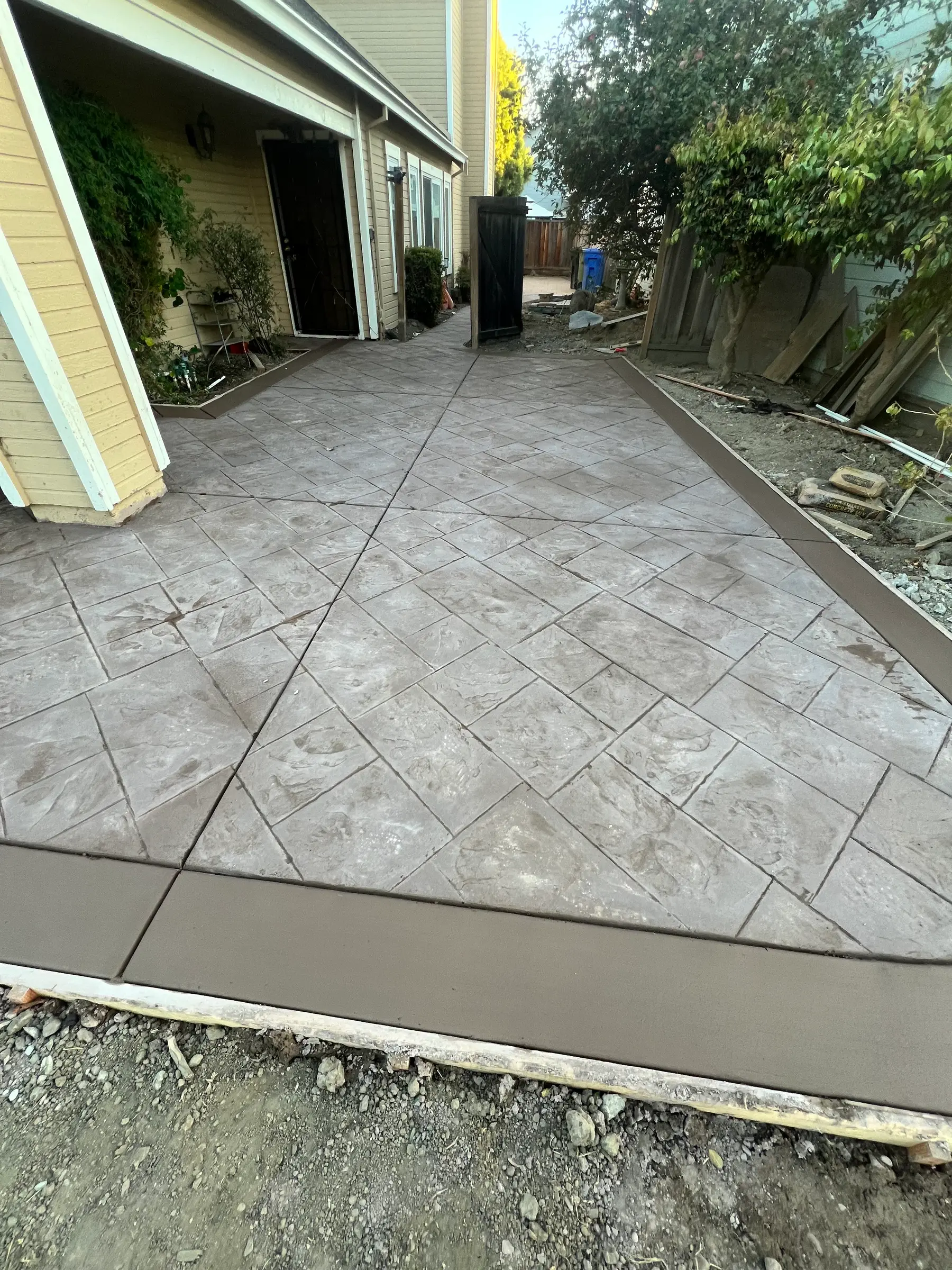 Stamped concrete side-yard walkway running to the garage door, framed by a brown banded border