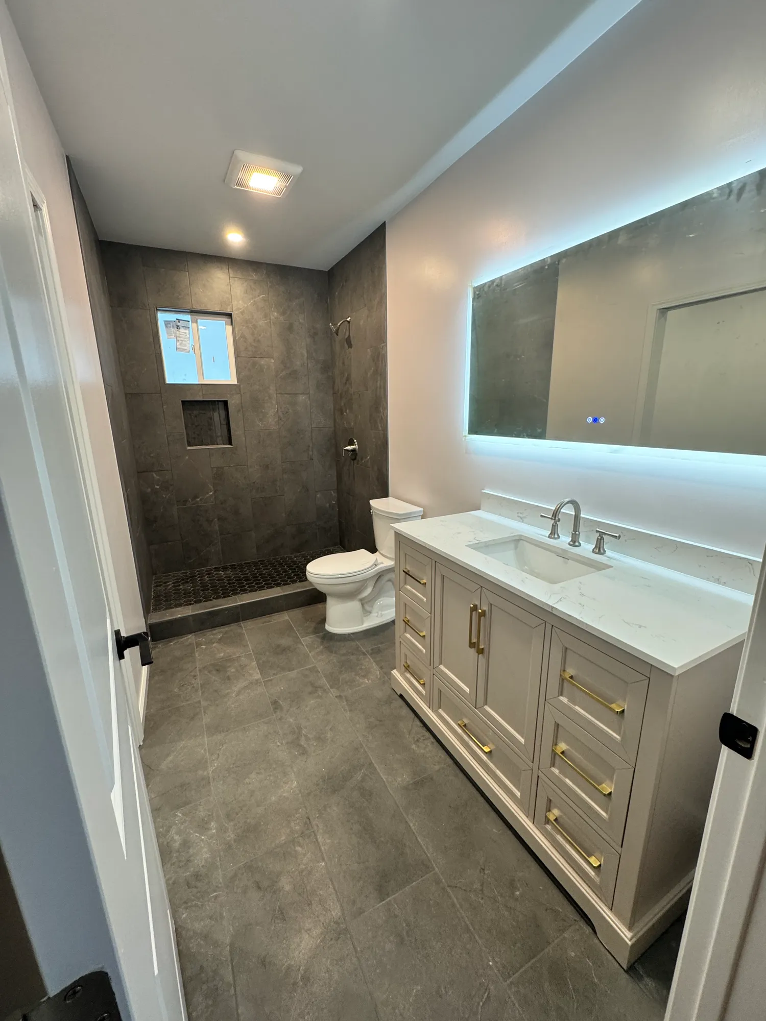 Bathroom remodel with gray stone-look tile, a walk-in shower, and an LED backlit mirror above a quartz vanity