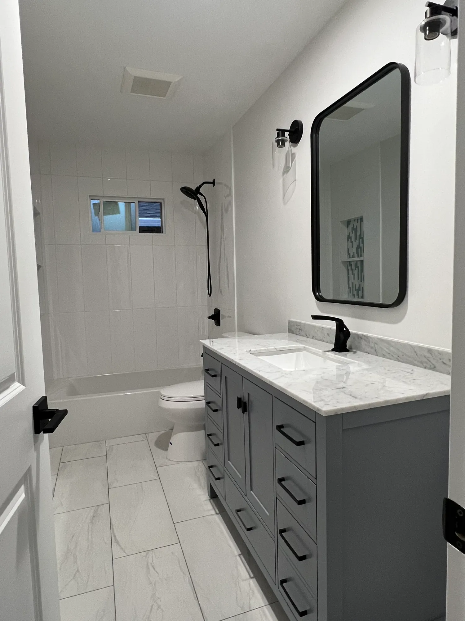 Guest bathroom with a gray shaker vanity, marble countertop, black framed mirror, and a tiled tub-shower