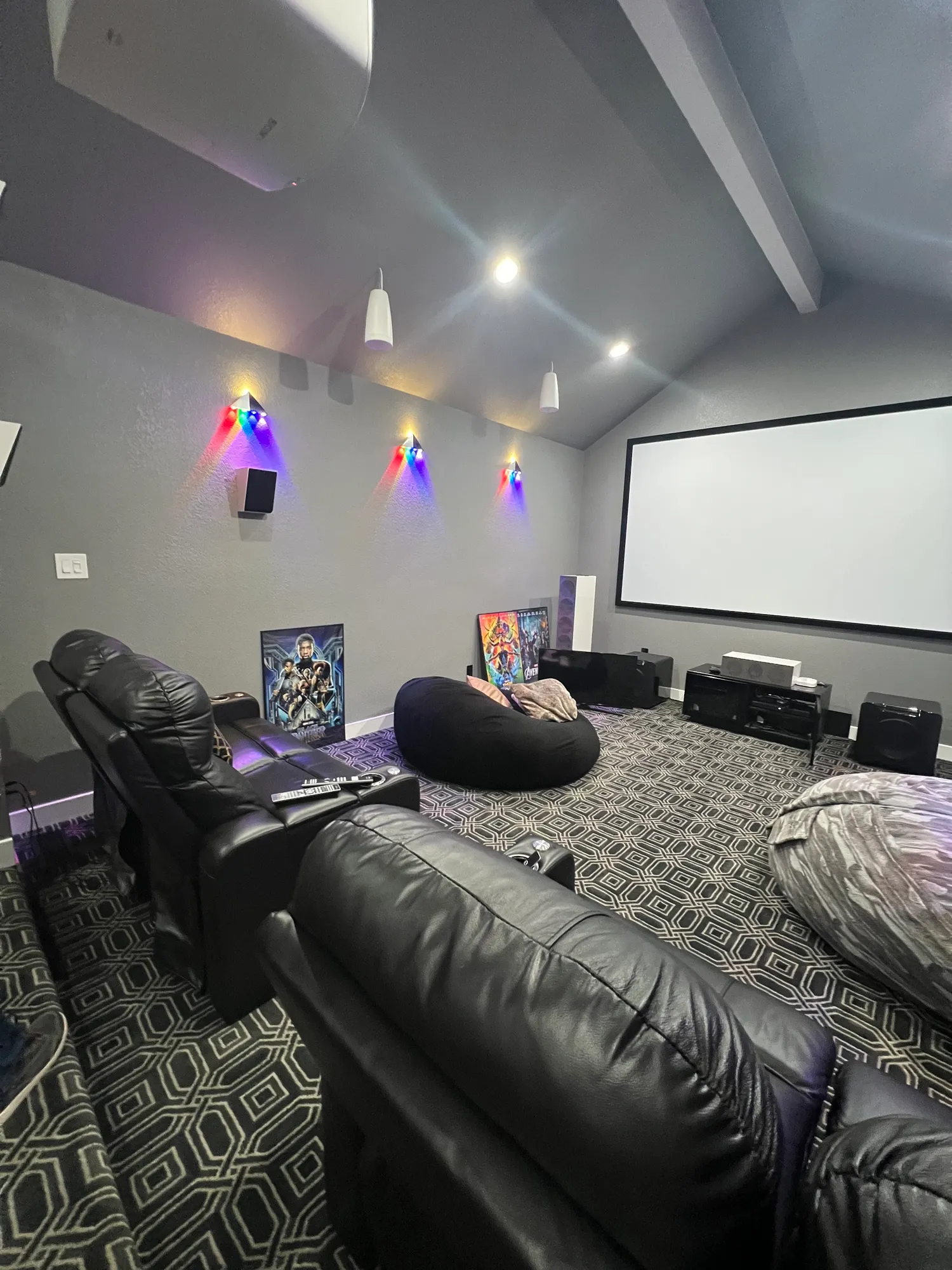 Finished home theater with a vaulted ceiling, projection screen, recliner seating, and accent sconces