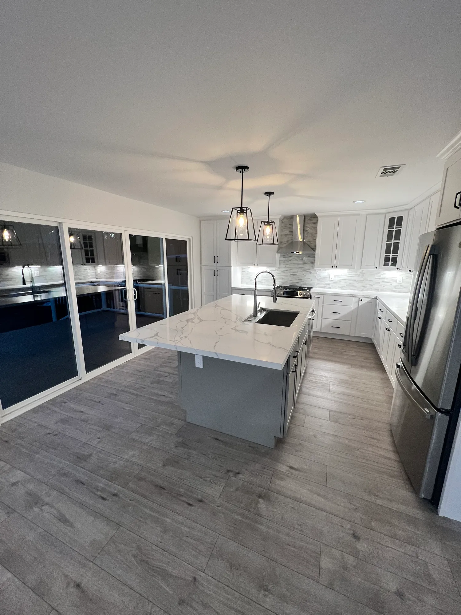 Kitchen remodel with white cabinetry, a quartz waterfall island, stainless appliances, and stone tile backsplash