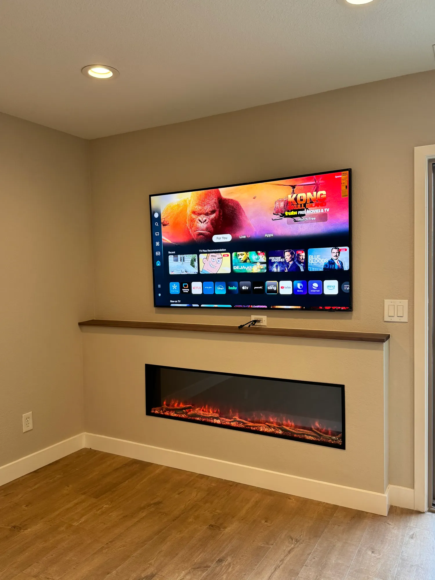 Living room feature wall with a recessed linear fireplace, walnut mantel shelf, and wall-mounted television