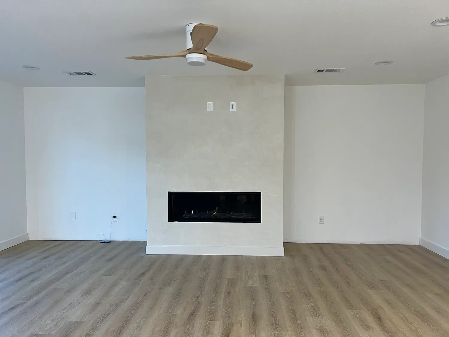 Living room with a full-height plaster fireplace surround, linear firebox, and new wide-plank flooring
