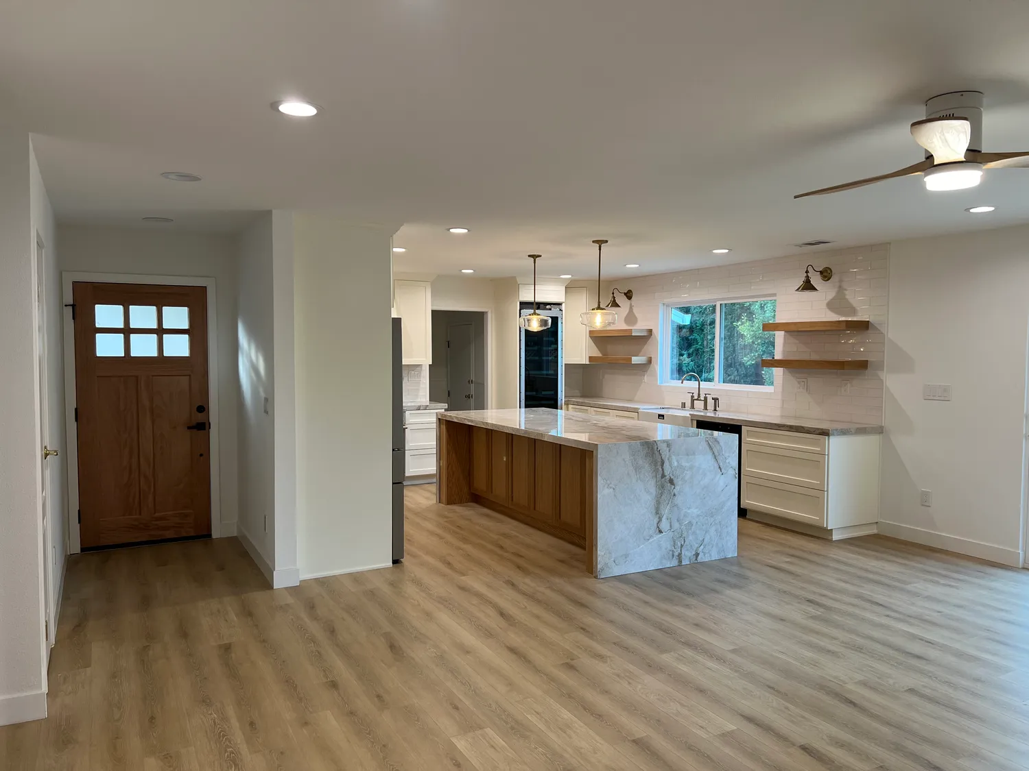 Open-concept remodel looking from the entry across new wide-plank flooring to the kitchen island and pendant lighting