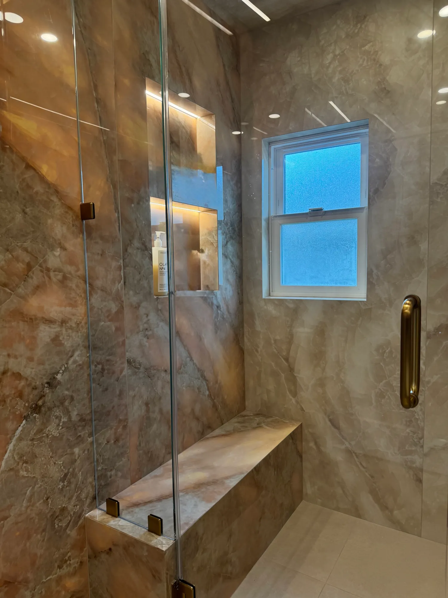 Quartzite slab shower with LED-lit niches, a full-width bench, and brushed gold hardware