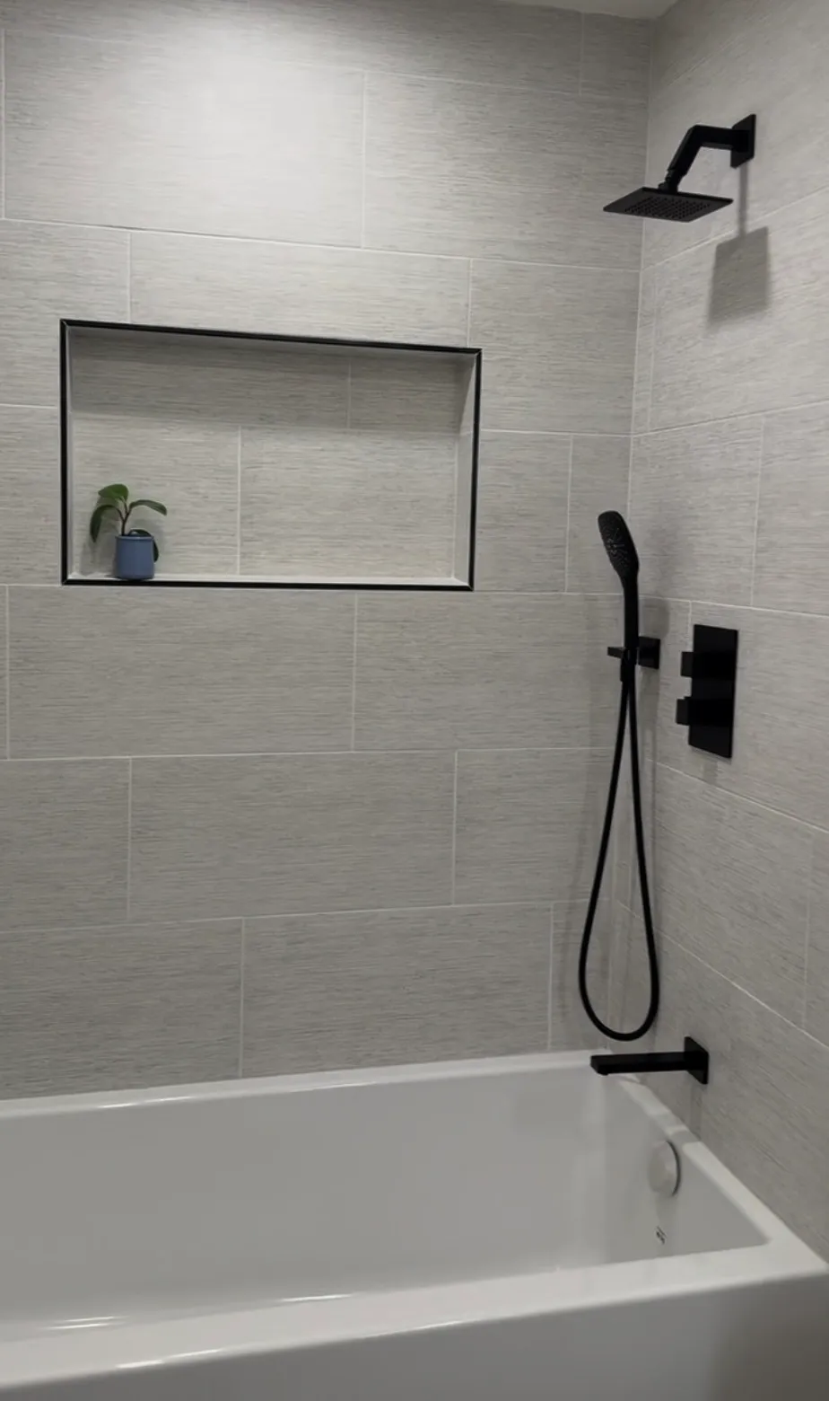 Tub and shower surround in linear gray tile with a recessed niche and matte black rain shower fixtures